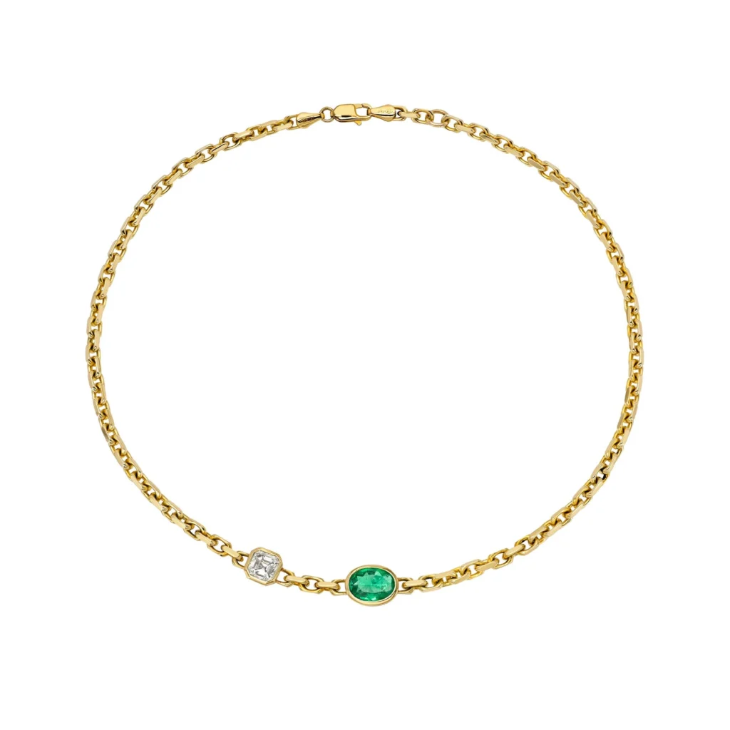 Gold chain necklace with emerald and diamond-like stones set along a thin links, on a white background, curved arc view.